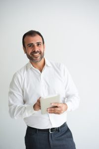 Portrait of cheerful mid adult businessman using digital tablet. Caucasian bearded man wearing white shirt looking at camera and smiling. Modern technology in business concept