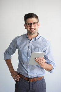 Portrait of happy businessman with digital tablet. Young Caucasian man wearing blue shirt and glasses looking at camera and smiling. Modern technology concept